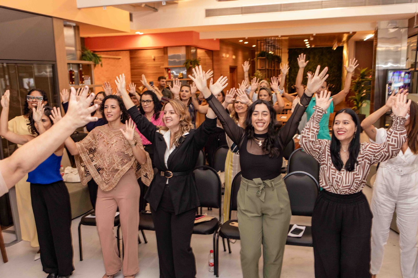 Mulheres do Clube EVA celebrando em evento presencial com as mãos para cima